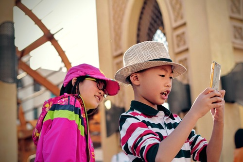 a photo of two kids looking into an Iphone- world of Social Media