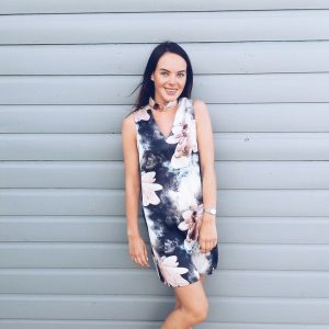 A picture of a girl in a pink dress standing by a grey wall